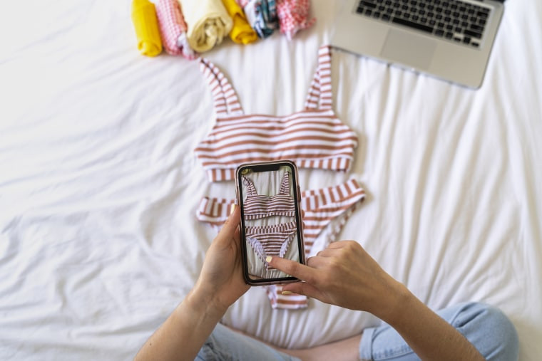 Woman photographing clothing on a bed for a Buy Nothing post.