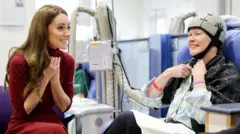 alt text: Kate Middleton, Princess of Wales, sits with a patient at the Royal Marsden Hospital, offering comfort and support during her visit.