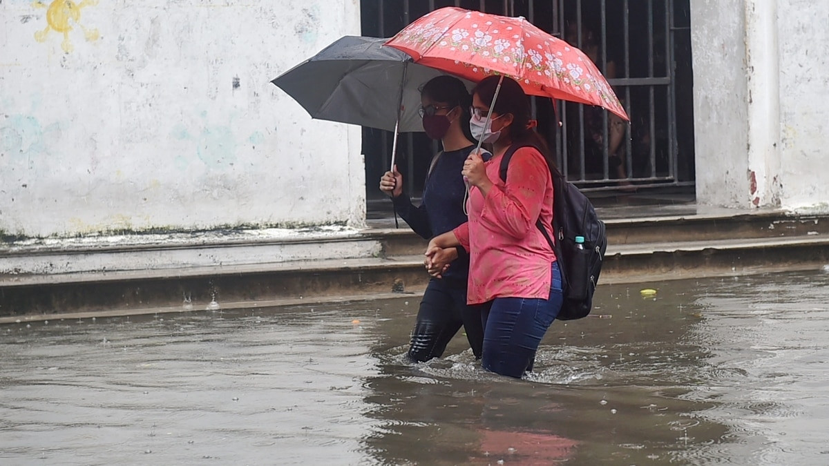 Alt: Flooded street in Kolkata with commuters wading through water after heavy rainfall.